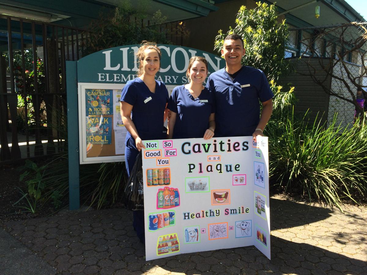 Dental students with presentation poster board on cavities and plaque.